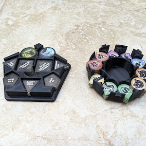 Op de afbeelding: Twee 3D-geprinte organizers voor een bordspel. De eerste organizer heeft een vijfhoekige vorm met vakken die zijn gelabeld met "Item Pile", "Sanity Roll" en "Item 10". De tweede organizer is een cirkel met vakken voor verschillende gekleurde tokens.