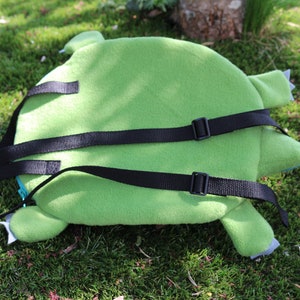 May include: Green plush backpack with adjustable black straps. The backpack is shaped like a turtle with a green shell and brown legs.