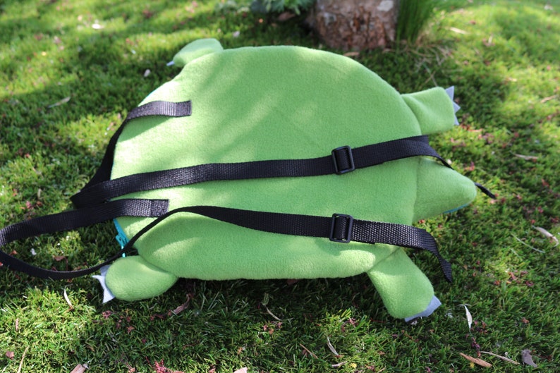 May include: Green plush backpack with adjustable black straps. The backpack is shaped like a turtle with a green shell and brown legs.