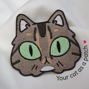Könnte beinhalten: Gestickter Bügel-Patch mit einem braunen Tabby-Kater mit grünen Augen. Der Text "Your cat as a patch" steht unter dem Kater.
