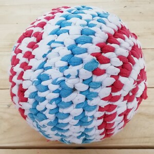 Puede incluir: Una pelota de crochet roja, blanca y azul hecha de recortes de tela. La pelota es un juguete para perros.