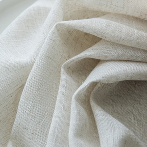 May include: Close-up of a white linen fabric with a textured weave. The fabric is folded and draped, showing its soft and natural texture.