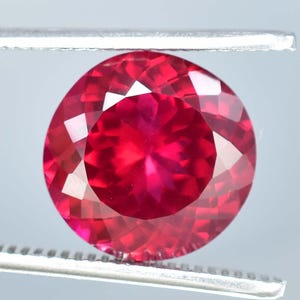 Peut inclure: Une pierre précieuse de rubis rouge vif avec une taille ronde et une surface facetée. Le rubis est serti dans un sertissage argenté.