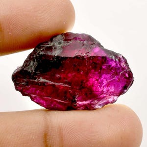 Puede incluir: Un gran cristal de amatista bruto de color púrpura oscuro, con una forma irregular y rugosa. El cristal es translúcido.