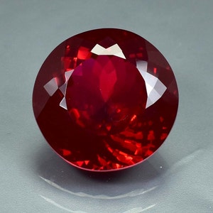 Peut inclure: Une pierre précieuse rouge foncé de taille ronde avec un éclat brillant.