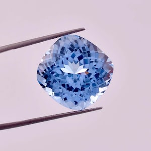 May include: A light blue cushion-cut aquamarine gemstone held by tweezers.