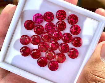 May include: A collection of 25 round, red gemstones in a white square box. The gemstones are arranged in a heart shape.