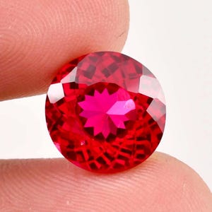Può includere: Una pietra preziosa rotonda di colore rosso brillante con un motivo a forma di stella al centro.