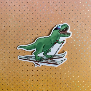May include: A green cartoon dinosaur wearing blue goggles and skiing down a slope. The dinosaur is on skis with the text "SKI-REX" and "BRUNT CARLSON DESIGN". The background is orange with small silver dots.