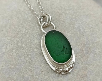 Op de afbeelding: Een zilveren ketting met een hanger van groen zeeglas. De hanger is gezet in een zilveren bezel met een geperlde rand.