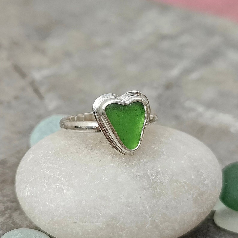 Op de afbeelding: Een zilveren ring met een groen, hartvormig stuk zeeglas in het midden.