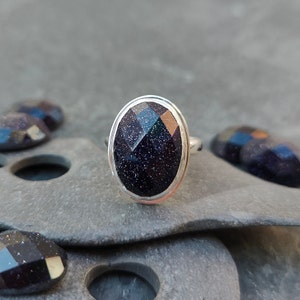 Puede incluir: Un anillo de plata con una piedra ovalada de color azul oscuro. La piedra tiene una superficie texturizada y brillante.