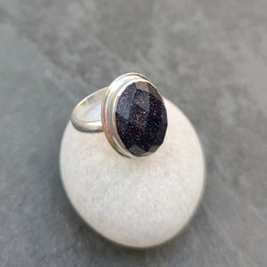 Puede incluir: Un anillo de plata con una piedra ovalada de color azul oscuro. La piedra tiene una superficie texturizada y brillante.