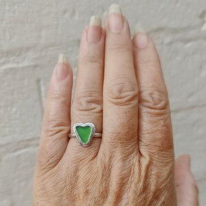 Op de afbeelding: Een zilveren ring met een groen, hartvormig stuk zeeglas dat in het midden is gezet.