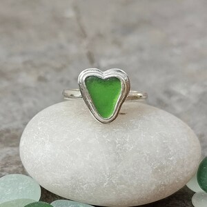 Op de afbeelding: Een zilveren ring met een groen, hartvormig stuk zeeglas in het midden.