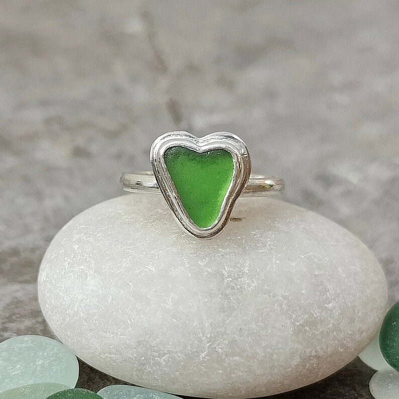 Op de afbeelding: Een zilveren ring met een groen, hartvormig stuk zeeglas in het midden.