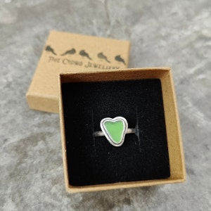 Op de afbeelding: Een zilveren ring met een groene hartvormige steen in het midden. De ring zit in een klein bruin doosje met de tekst "Five Crows Jewellery" op de deksel.