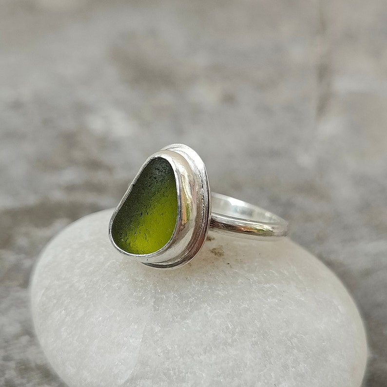 May include: A silver ring with a green sea glass stone set in a bezel setting.
