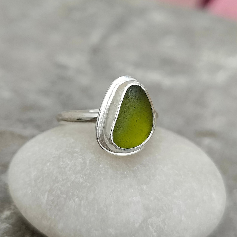 May include: A silver ring with a green sea glass stone set in a bezel setting.