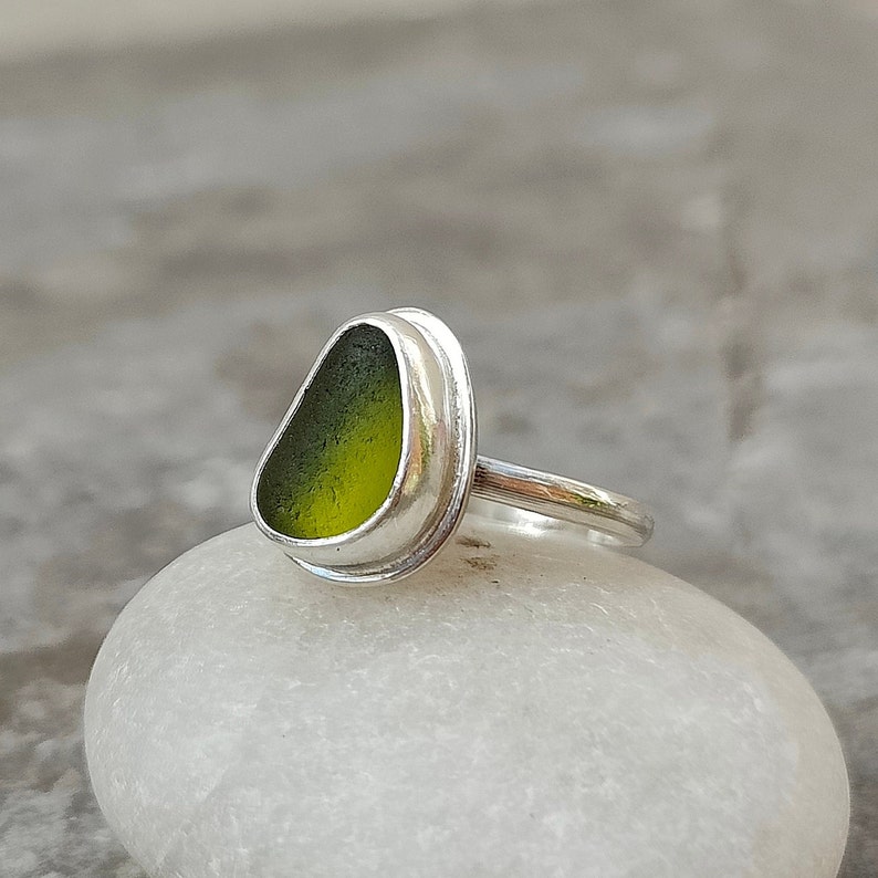 May include: A silver ring with a green sea glass stone set in a bezel setting.