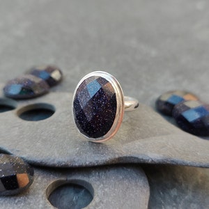 Puede incluir: Un anillo de plata con una piedra ovalada de color azul oscuro. La piedra tiene una textura brillante y moteada.