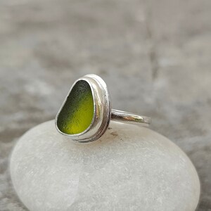 May include: A silver ring with a green sea glass stone set in a bezel setting.