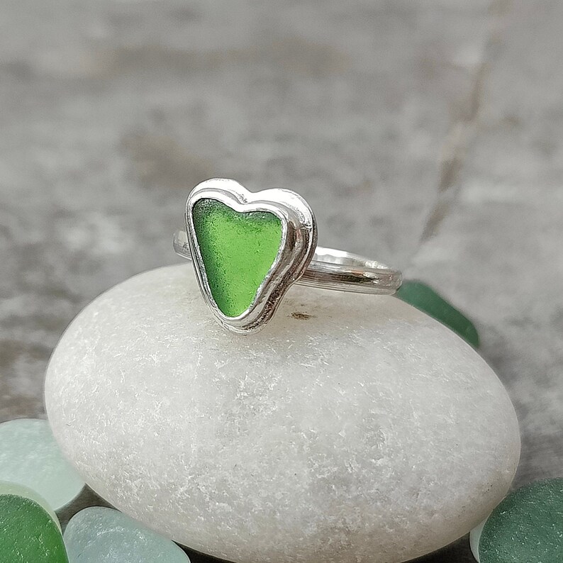 Op de afbeelding: Een zilveren ring met een groen, hartvormig stuk zeeglas in het midden.