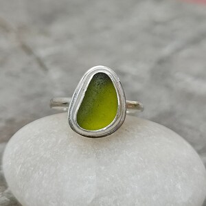 May include: A silver ring with a green sea glass stone set in a bezel setting.