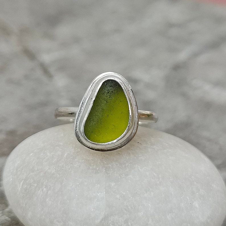 May include: A silver ring with a green sea glass stone set in a bezel setting.