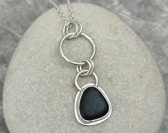 以下が含まれることがあります： 黒い石のペンダントが付いたシルバーネックレス。ペンダントは、ダブルサークルデザインのシルバーフレームにセットされています。