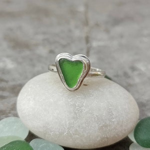 Op de afbeelding: Een zilveren ring met een groen, hartvormig stuk zeeglas in het midden.
