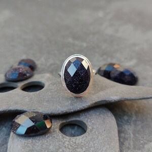 Puede incluir: Un anillo de plata con una piedra ovalada de color azul oscuro. La piedra tiene una superficie texturizada y brillante.