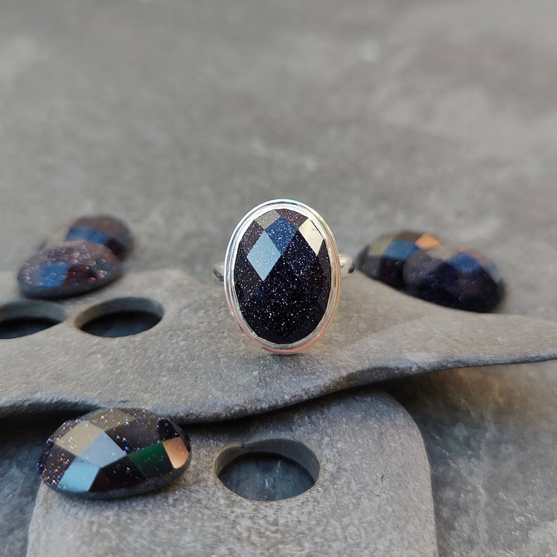 Puede incluir: Un anillo de plata con una piedra ovalada de color azul oscuro. La piedra tiene una superficie texturizada y brillante.