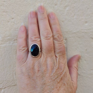Puede incluir: Un anillo de plata con una piedra ovalada de color azul oscuro engastada en un engaste de plata.