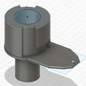 Pode incluir: Uma peça de plástico cinza impressa em 3D com uma base cilíndrica e uma extensão retangular plana. O cilindro tem uma abertura circular na parte superior.