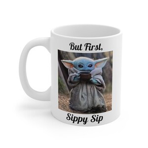 K&ouml;nnte beinhalten: Eine wei&szlig;e Keramiktasse mit einem Motiv eines Baby Yoda-Charakters, der aus einer Tasse trinkt. Der Text "But First, Sippy Sip" ist auf die Tasse gedruckt.