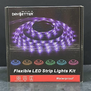 May include: A black product box for a DAYBETTER Flexible LED Strip Lights Kit. The box features a large coil of purple LED lights, smaller coils in blue, yellow, red, green, teal, and pink, and icons for power, RGB, and durability with text.