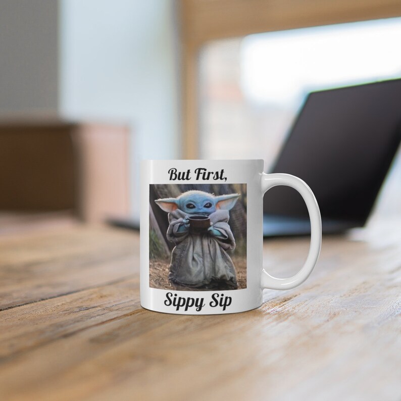 K&ouml;nnte beinhalten: Wei&szlig;e Keramiktasse mit einer blauen Figur, die eine Tasse h&auml;lt, und dem Text "But First, Sippy Sip".