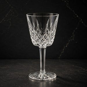 May include: A clear crystal wine glass featuring a detailed diamond-cut pattern on the bowl, a slender stem, and a circular base with a radial sunburst design. The glass is transparent and reflects light through its intricate geometric facets.