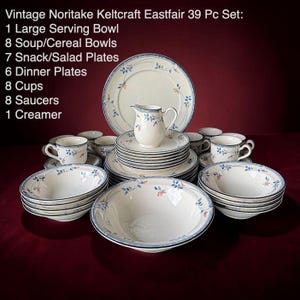 May include: A 39-piece Noritake Keltcraft Eastfair dinnerware set featuring cream-colored ceramic with blue rims and delicate orange and blue floral accents. The set includes a large serving bowl, soup bowls, salad plates, dinner plates, cups, saucers, and a creamer.
