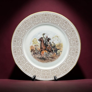 May include: A white porcelain decorative plate featuring a central illustration of a person on horseback waving a hat, accompanied by other riders in a field. The plate has a wide border with an intricate gold filigree pattern and a gold rim.