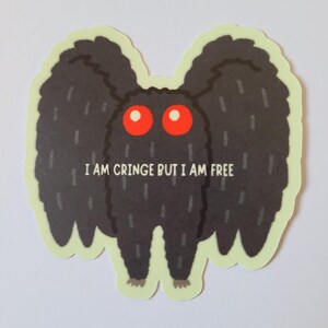 Könnte beinhalten: Ein Aufkleber mit einer Cartoon-Motte mit großen, federartigen Flügeln und roten Augen. Die Motte ist schwarz mit einem hellgrünen Rand und dem Text "I AM CRINGE BUT I AM FREE".