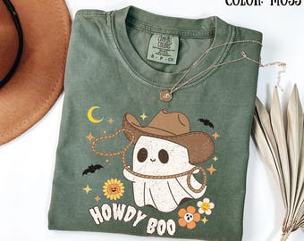 May include: A green t-shirt with a cartoon ghost wearing a cowboy hat and lasso. The ghost is white with black eyes and a smile. The text "Howdy Boo" is printed below the ghost.