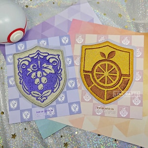 May include: Two iron-on patches featuring embroidered crests. The left patch is purple and white with a grapevine design. The right patch is yellow and brown with a citrus fruit design. Both patches have the text "iron-on patch by LINCRAFTS".