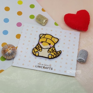 May include: Iron-on patch featuring a yellow and brown cartoon animal with a cute expression. The patch is on a white card with the text "Iron-on patch by LINCRAFTS" and "LINCRAFTS" in the bottom right corner.