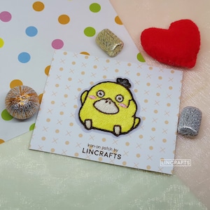 May include: Iron-on patch featuring a yellow embroidered cartoon chick with black eyes, a black beak, and a black hat. The patch is on a white card with a white and orange polka dot background. The text "iron-on patch by LINCRAFTS" is printed on the card.