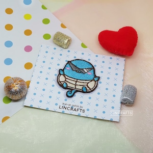 May include: An iron-on patch featuring a blue cartoon character wearing sunglasses and a white life vest. The patch is on a white card with blue polka dots and the text "Iron-on patch by LINCRAFTS".