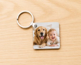 May include: Square keychain featuring a smiling baby and a golden retriever. The image is attached to a silver metal keyring. The background is a light wood surface.