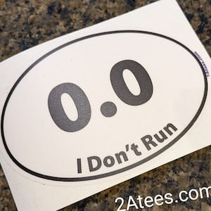 May include: White oval sticker with black text. The text reads "0.0 I Don't Run" and "2Atees.com".