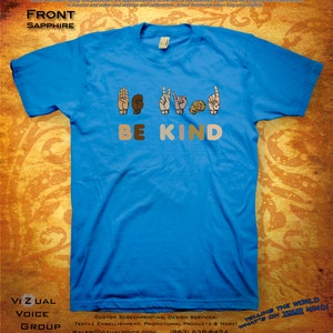 May include: A blue t-shirt with the words "BE KIND" in colorful letters and a sign language interpretation of the phrase above the words. The sign language is depicted with five hands in different skin tones.